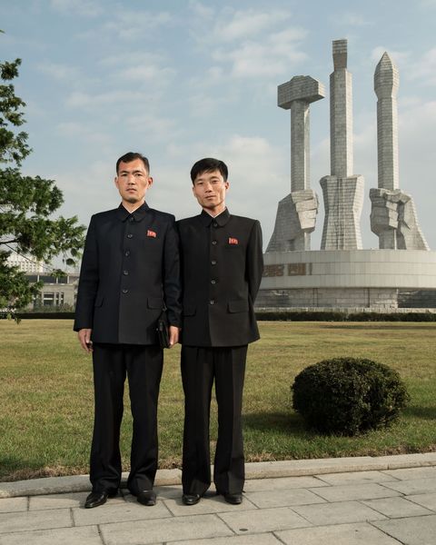 Twee kantoormedewerkers staan voor het Monument voor de Oprichting van de Partij in Pyongyang De hamer sikkel en kalligrafiekwast staan symbool voor de arbeiders de boeren en de intellectuelen