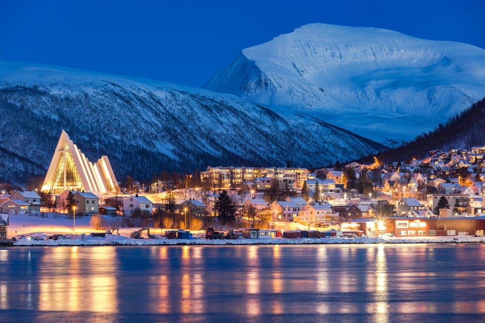 dusk over snowy mountains overlooking the arctic cathedral and traditional houses mirrored in the icy fjord, tromso, norway