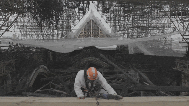 Een werknemer verwijdert puin onder de verwrongen steigers op het dak van de kathedraal Het volledige gezichtsmasker beschermt arbeiders tegen het giftige stof dat ontstond toen de loden dakplaten tijdens de brand smolten