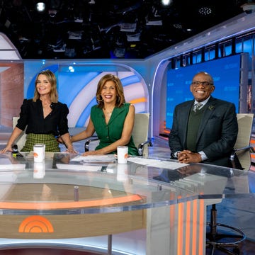 news anchors seated at a modern broadcasting desk with a partially visible background