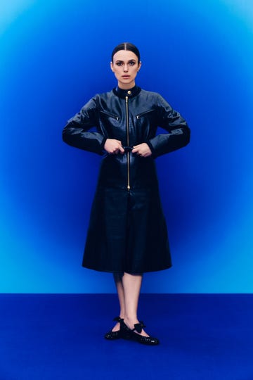 a person wearing a black leather coat and black shoes against a blue background