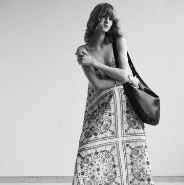 a person wearing a patterned dress stands with a bag on their shoulder a person wearing a patterned dress stands with a bag on their shoulder