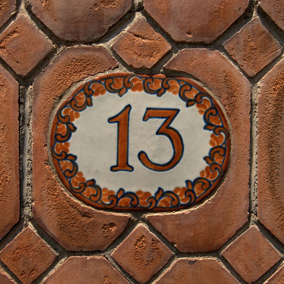 number 13 street address handpainted on a glazed tile on a eroded terracotta tile wall