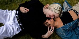 two women laughing and kissing lying on grass