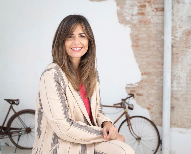 la presentadora con un traje de rayas en color beige y camiseta color coral sonríe a la cámara