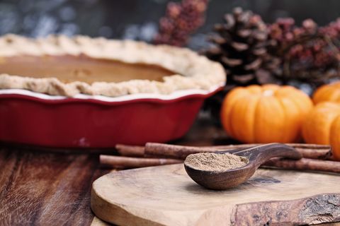 pumpkin pie spice measured in a wooden spoon over a rustic wooden background pie and pumpkins in the background