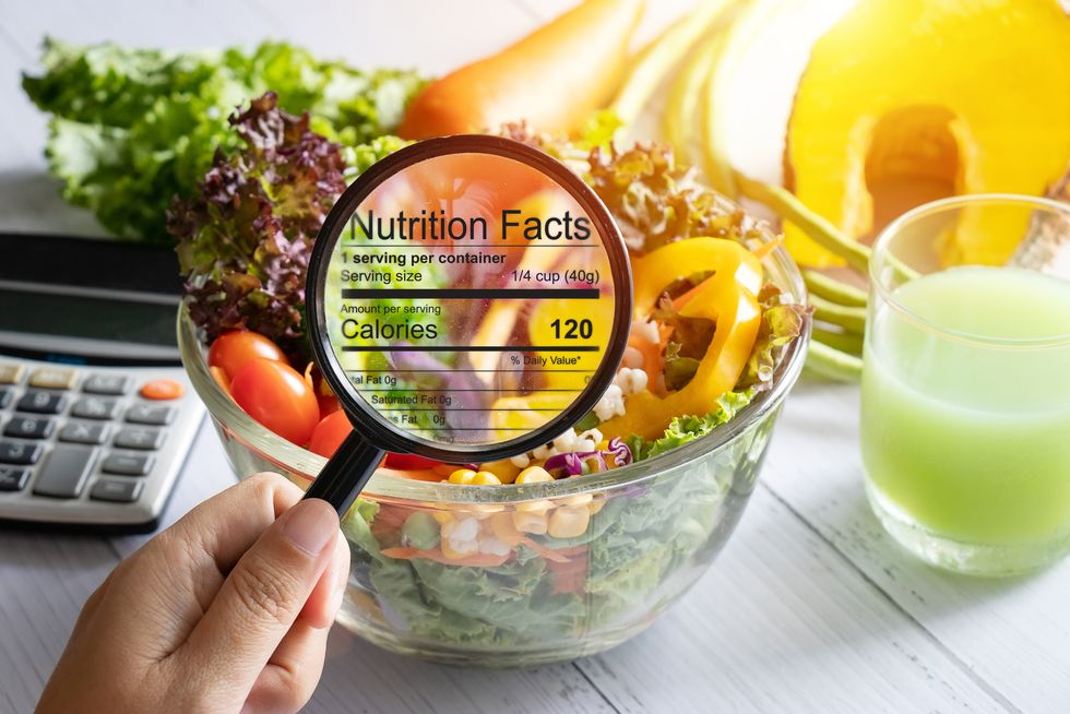 nutritional information concept hand use the magnifying glass to zoom in to see the details of the nutrition facts from food , salad bowl