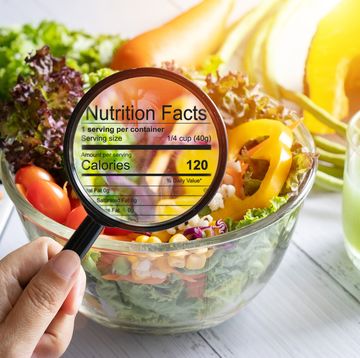nutritional information concept hand use the magnifying glass to zoom in to see the details of the nutrition facts from food , salad bowl