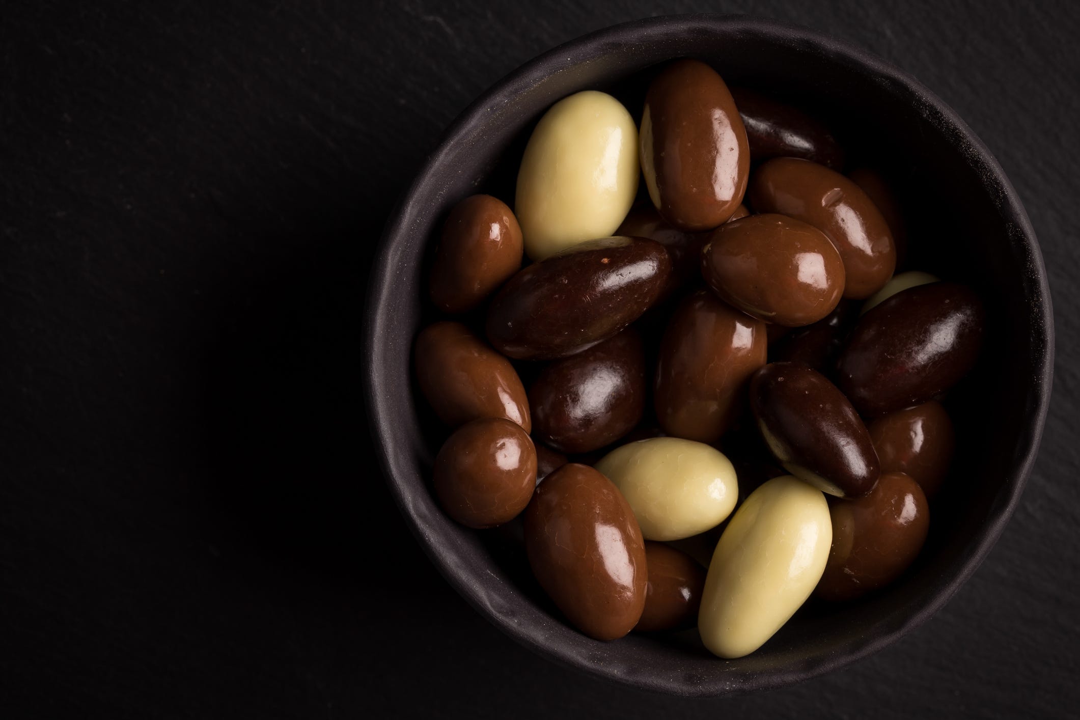 almonds in white, dark, milk chocolate in a bowl on stone board