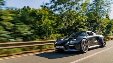 a black sports car driving on a road with trees on either side
