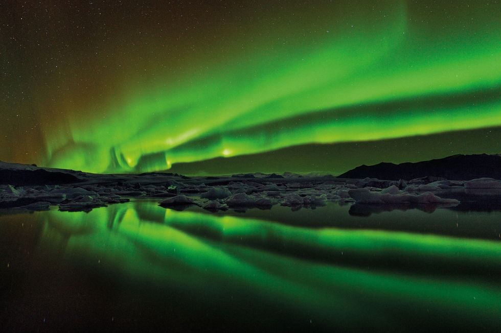 In het IJslandse gletsjermeer Jokulsarlon drijven ijsschotsen onder het magische noorderlicht Het poollicht verschijnt wanneer de zonnewind botst met de magnetosfeer van de aarde dat de aarde beschermt tegen straling van de zon en erop meedrijft wat zorgt voor prachtige taferelen op grote hoogten