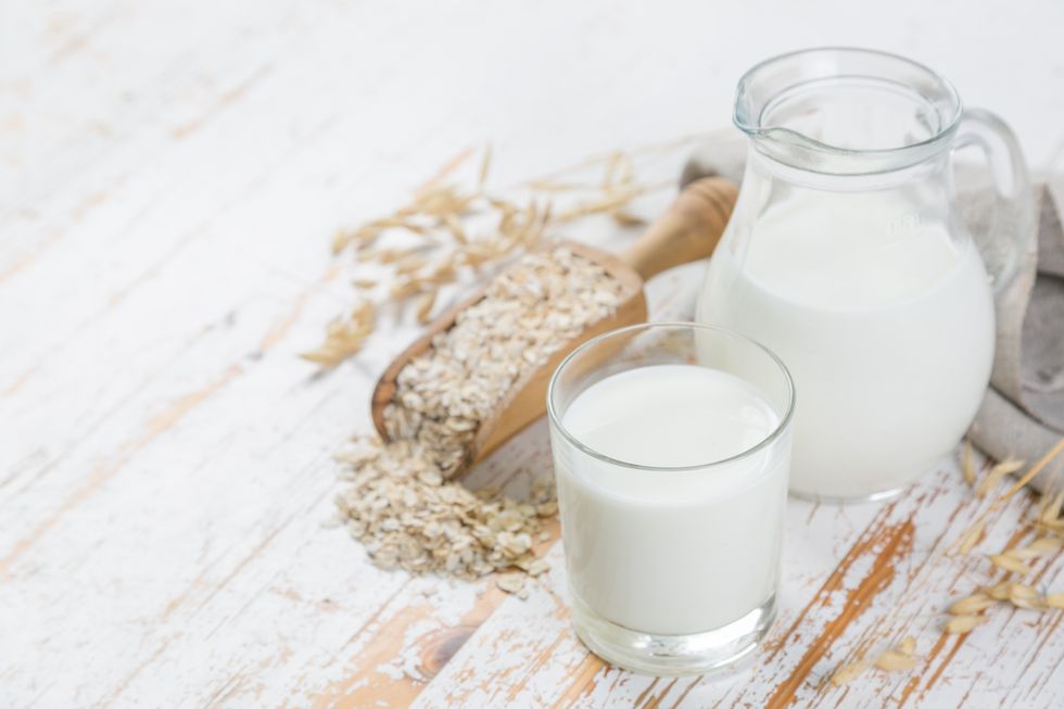 Oat milk in glass and jar on wood background