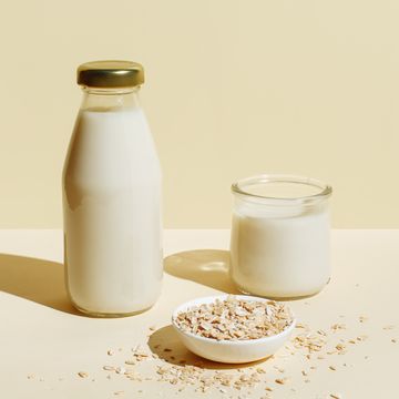 oat milk in glass bottle and glass, oatmeal in a white bowl on beige background healthy vegan non dairy organic drink with flakes lactose free milks in minimal flat lay style top view, copy space