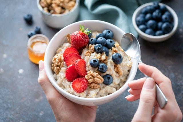 hands holding bowl of oatmeal with berries and nuts