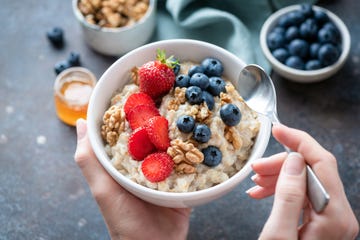 hands holding bowl of oatmeal with berries and nuts