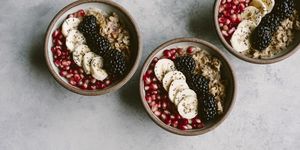 3 oatmeal bowls topped off with blackberry, banana, and pomegranate seeds are photographed from the top view.