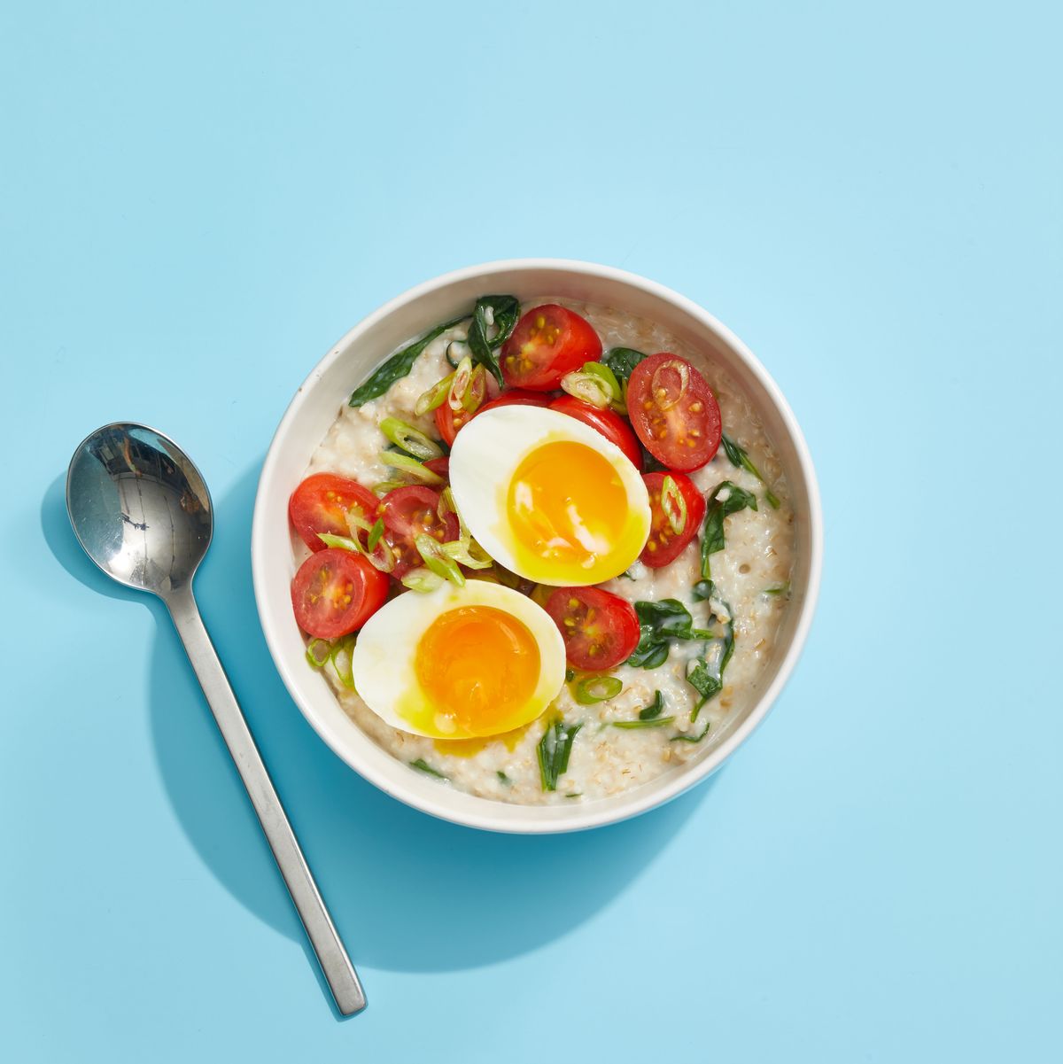 oatmeal with greens and eggs on blue background with spoon