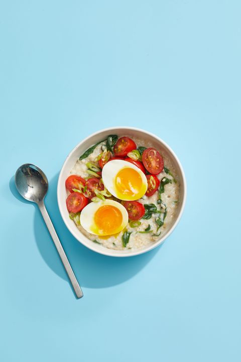 oatmeal with greens and eggs on blue background with spoon