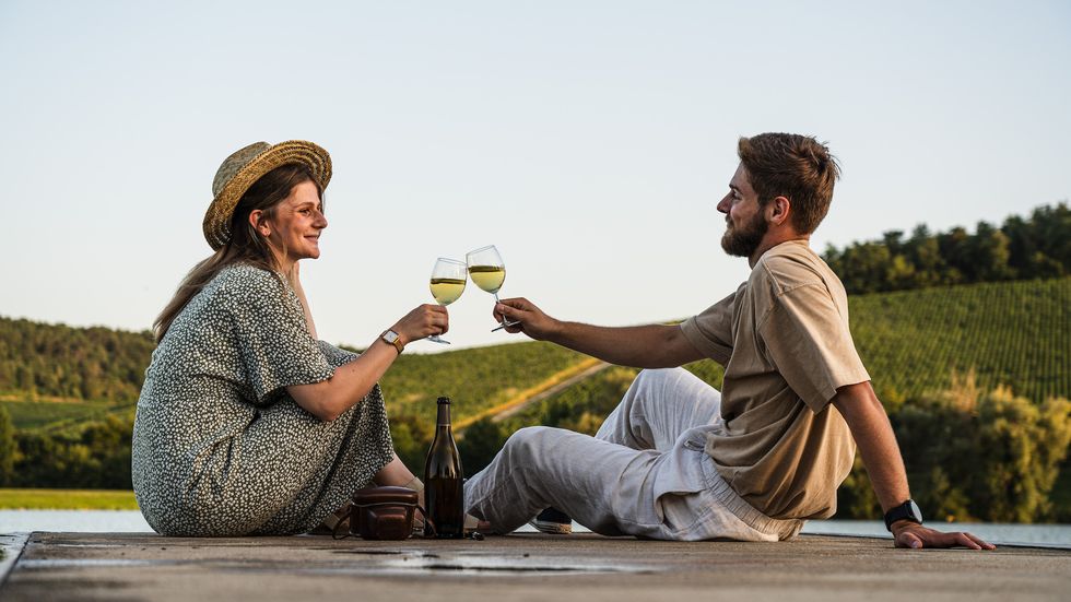 a man and woman sitting on a bench with wine glasses