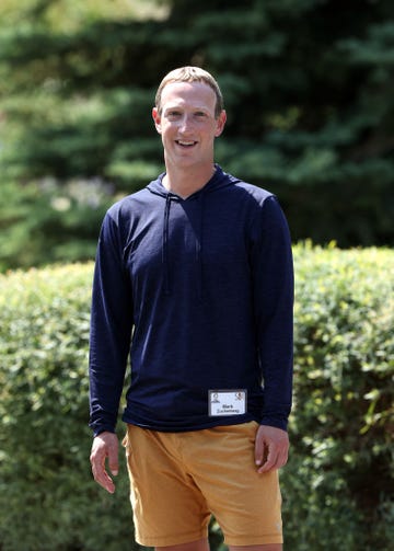 mark zuckerberg stands outside and smiles at the camera, he is wearing a long sleeve navy blue hoodie