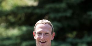 mark zuckerberg stands outside and smiles at the camera, he is wearing a long sleeve navy blue hoodie