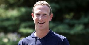 mark zuckerberg stands outside and smiles at the camera, he is wearing a long sleeve navy blue hoodie