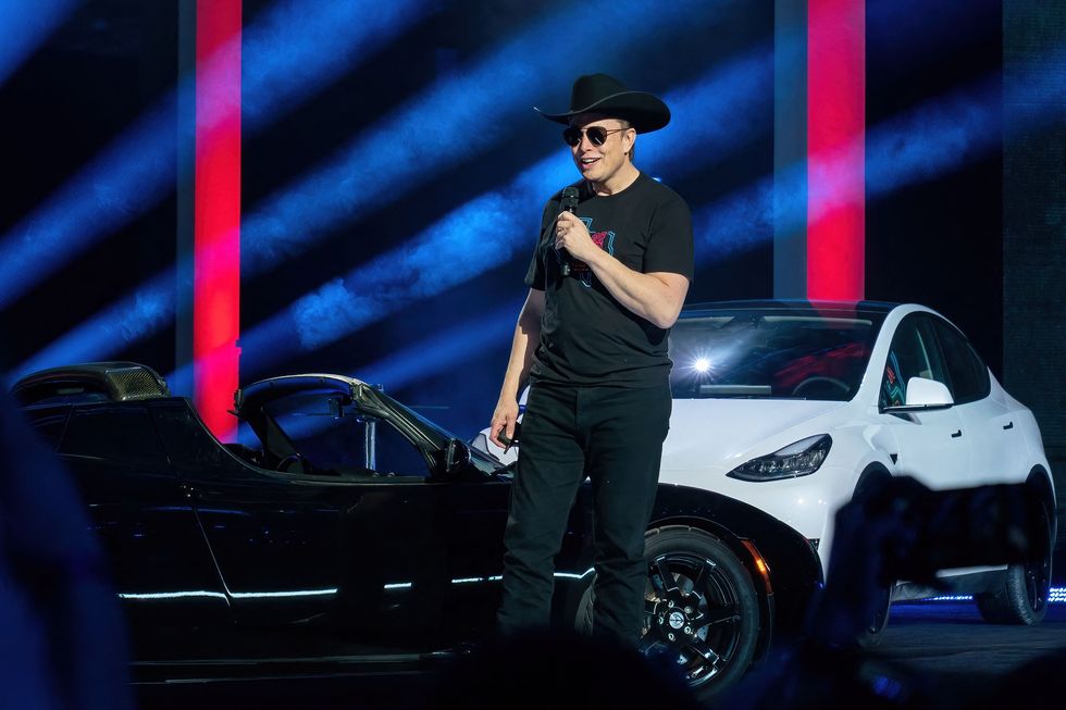 elon musk at tesla giga texas with white model y and black roadster