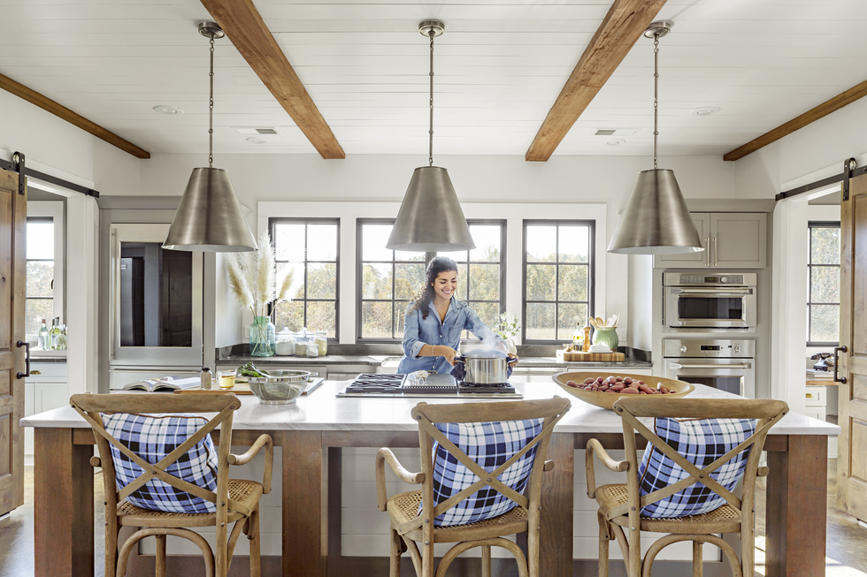 off white rustic kitchen with steel gray fixtures and natural wood rafters, island, chairs, and sliding barn doors