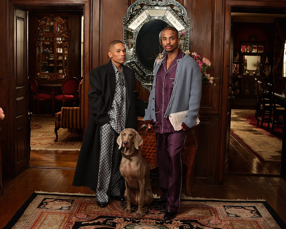 two individuals in elegant loungewear pose with a large dog in a richly decorated interior
