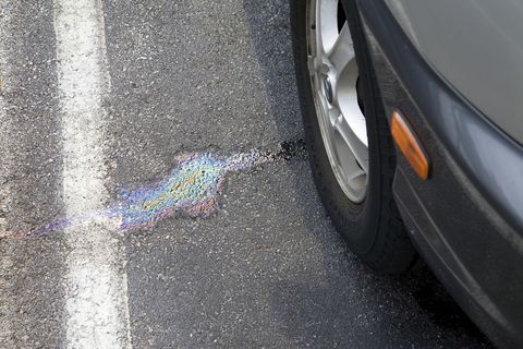 Oil spot on asphalt next to car wheel
