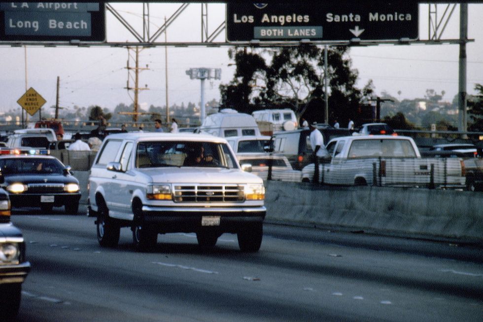 a white ford bronco drives on a highway with one car behind it and many cars stopped in the opposite direction