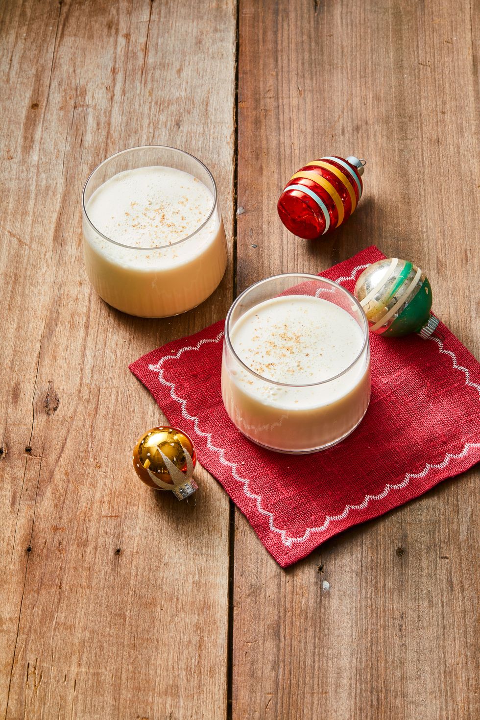 two glasses of old fashioned eggnog with christmas ornaments on the side