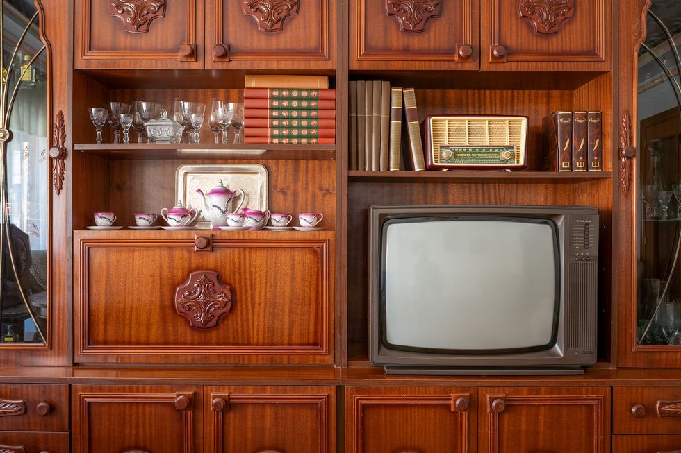 old television and radio on a wooden furniture with books, teacups and glasses in a 1980s style living room, showcasing a nostalgic glimpse into the past.