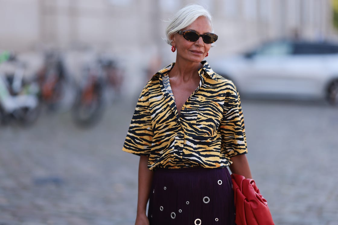 copenhagen, denmark august 07 grece ghanem is seen wearing oval tortoiseshell sunglasses from prada, red hoop earrings with a white dot pattern, and a shirt with wide sleeves in a yellow and black tiger print, a structured red leather clutch with a gathered silhouette inspired by a rose from burberry, and a dark purple knee length fringed skirt with silver eyelet embellishment in different sizes from prada, before the garment show during day three of the copenhagen fashion week cphfw ss25 on august 07, 2024 in copenhagen, denmark photo by jeremy moellergetty images