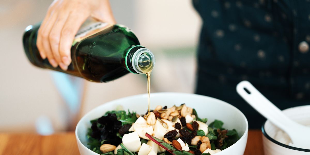 person pouring olive oil on salad