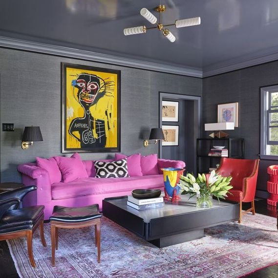 living room with long pink sofa and red leather wing hair and blue leather armchair on either side and a low pedestal block table and picasso esque painting on the wall behind