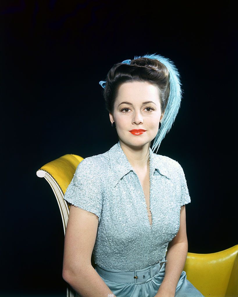 olivia de havilland, british actress, wearing a blue dress with a matching blue feather in her hair, sitting on a yellow sofa in a studio portrait, against a black background, circa 1935 photo by silver screen collectiongetty images