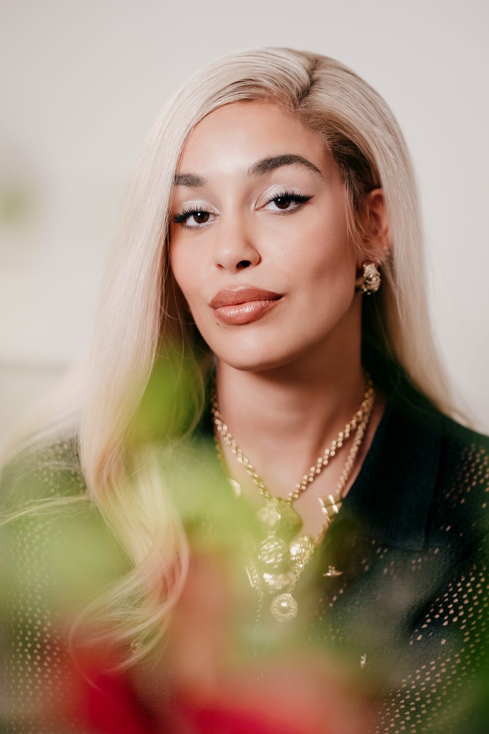 person with long blonde hair wearing jewelry partially obscured by foliage