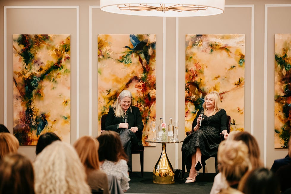 Discussion event featuring two individuals on stage with abstract artworks behind them