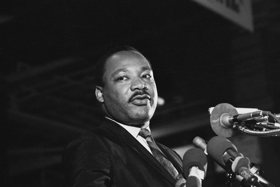 martin luther king jr speaks into several microphones and looks to the left, he wears a suit and tie