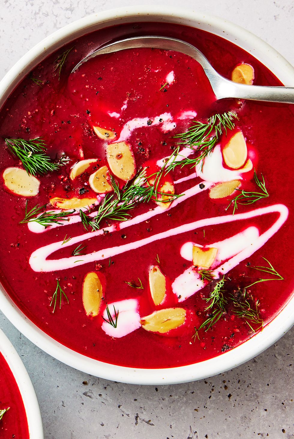 one pot harissa beet soup in a white bowl topped with almonds, herbs, and cream
