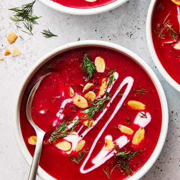 one pot harissa beet soup in a white bowl topped with almonds, herbs, and cream