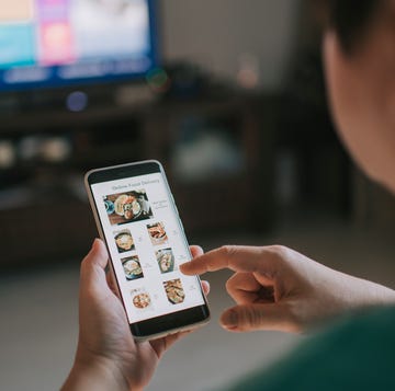 online food delivery mobile app shown on smart phone screen hold by asian woman hands in living room