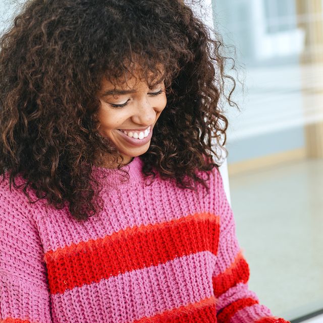 a woman in a vibrant eye catching pink and red jumper using a laptop