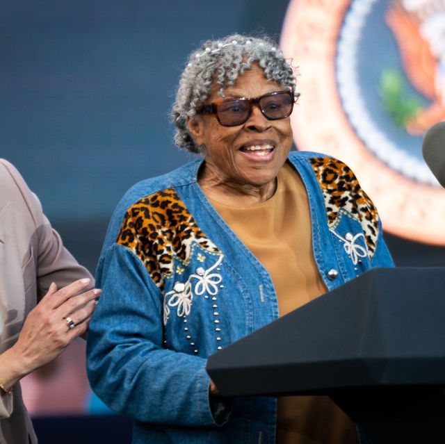opal lee, wearing a denim designed coat, yellow shirt, and sunglasses, speaks at a podium with two microphones and the us presidential seal, standing next to a laughing kamala harris