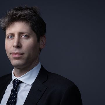 a man smiles slightly at the camera, he wears a suit coat, white collared, and polka dot tie