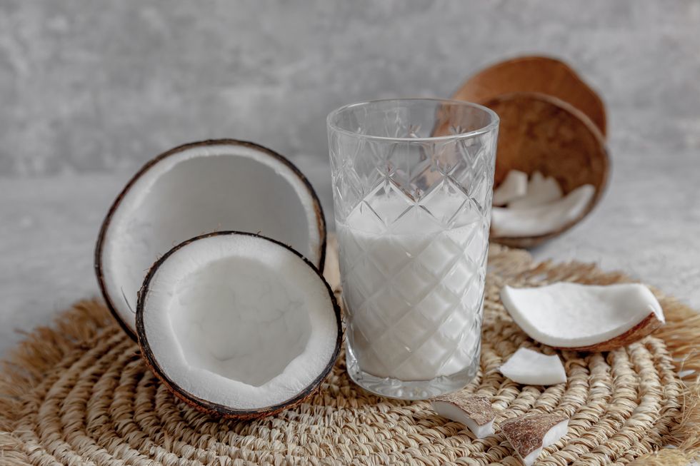 opened coconuts, glass of homemade coconut milk and coconut chunks