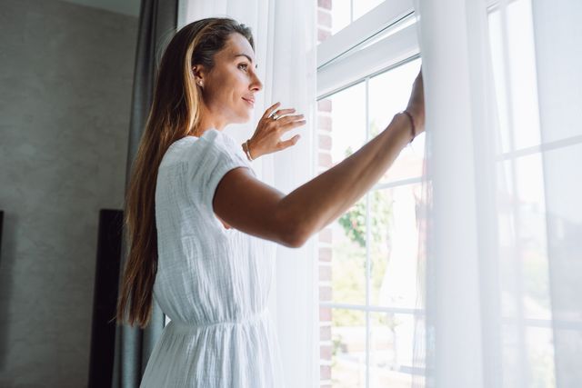 opening curtains and day beginnings. blonde long haired woman pulling curtains, open window, new beginnings of the day in the morning
