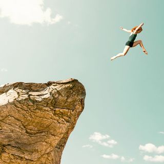 concept of determination, adrenaline and over coming fear woman jumps from one rock formation to another it is a dangerous jump and she uses all of her speed and strenght to make it across