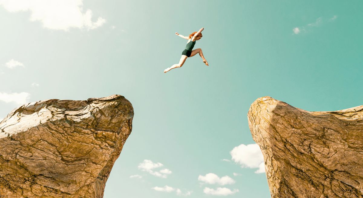 concept of determination, adrenaline and over coming fear woman jumps from one rock formation to another it is a dangerous jump and she uses all of her speed and strenght to make it across